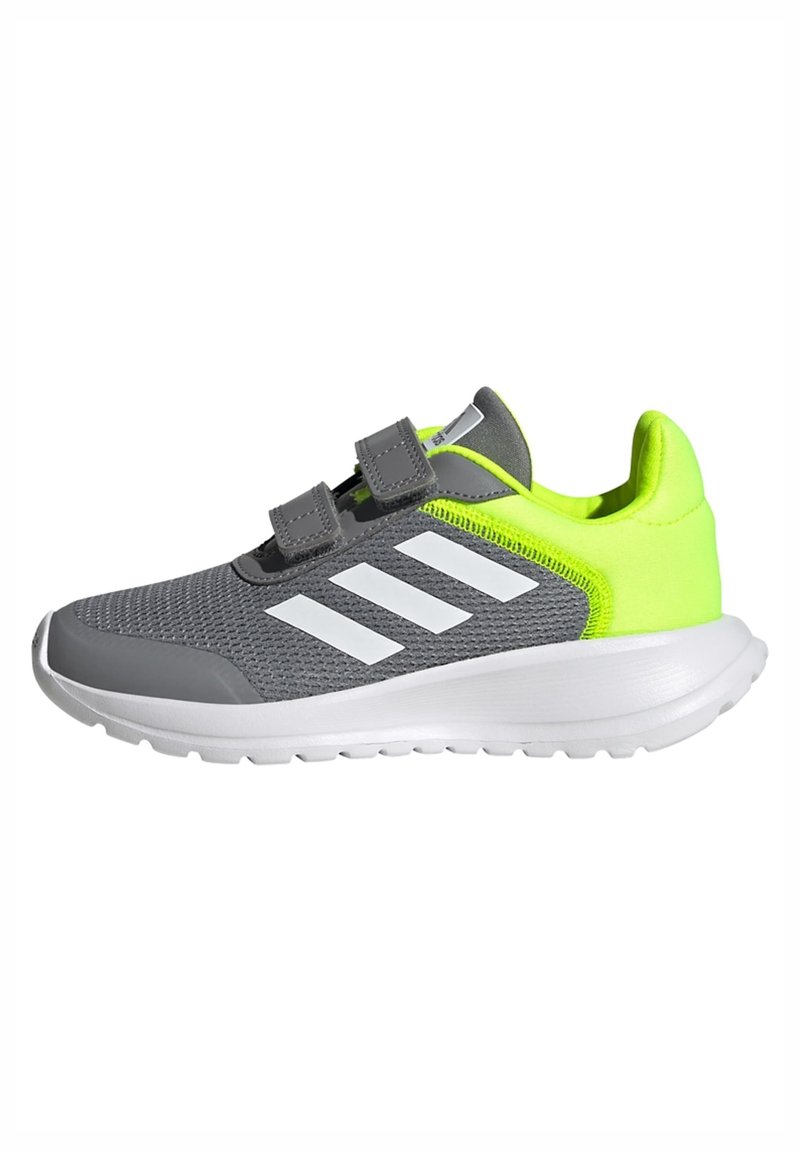 Chaussure de sport grise avec des accents vert néon lumineux, tige en mesh, rayures blanches et bandes Velcro. Semelle blanche flexible avec un relief texturé.
