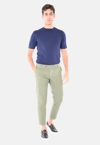 Maglietta a maniche corte a coste blu navy, pantaloni tapered verde oliva e scarpe slip-on nere con dettagli marroni. Il modello è in piedi su uno sfondo chiaro.