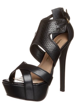 Sandalia negra de tacón alto con plataforma, tiras cruzadas en cuero liso y detalles texturizados, con un cierre elegante de hebilla.