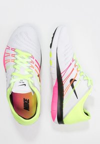 Sportovní tenisky Nike v bílé síťovině s neonově žlutými a růžovými akcenty. Mají zaoblenou špičku, flexibilní podrážku a texturovaný svršek s barevnými pruhy.