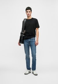 T-shirt preta de algodão com mangas curtas, jeans azul de denim e ténis cinzentos. Uma bolsa de ombro preta de pele pendura-se no ombro esquerdo.