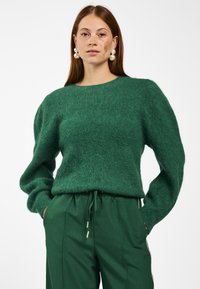 Groene, fluffy trui met lange, volumineuze mouwen en een ronde halslijn, gecombineerd met bijpassende groene broeken met zijstrepen.