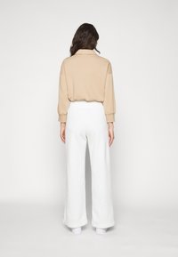 Beige kort sweatshirt med krage, kombinert med vide hvite bukser. Glatt stofftekstur. Synlig søm langs ermer og nederkant.