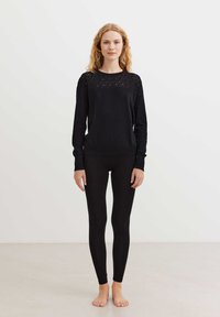Maglione nero con dettagli in pizzo sulle spalle, abbinato a leggings neri. Il maglione presenta un collo rotondo e polsini aderenti.