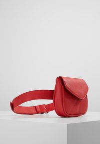 Punainen nahkavyölaukku, jossa on jämäkkä muotoilu, pyöreä muoto, läppä suljenta ja sileä pinta. Mukana säädettävä vyö.