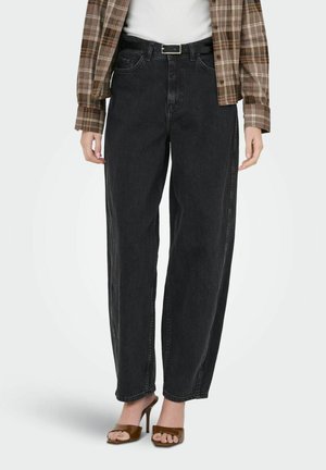 Femme portant un jean noir taille haute avec une ceinture noire, une chemise à carreaux marron, un haut blanc et des sandales à talons ouvertes marron.