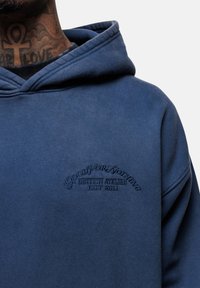 Felpa blu in cotone, con tasca a marsupio e logo ricamato sul petto. Il testo include "GOOD FOR NOTHING" e "EST 2011."