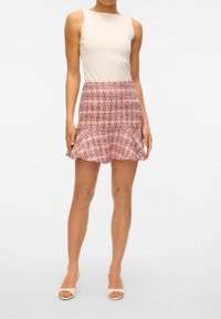 Débardeur beige ajusté associé à une jupe évasée rose avec un motif à carreaux noirs. Porté avec des sandales à talons ouvertes de couleur beige clair.
