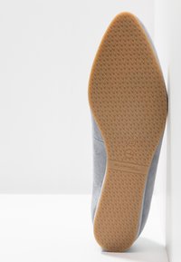 Semelle d'une chaussure gris clair avec une semelle en caoutchouc marron texturée indiquant la taille 37 et le nom de la marque "Tamaris".
