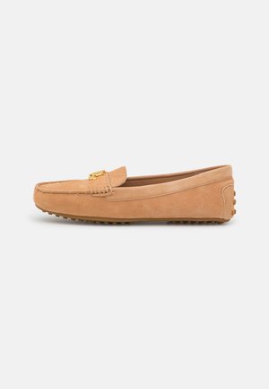 Tanfarvet ruskindslipper med guldfarvet metalspænde og gummisåle med nopret mønster, vist fra siden på en hvid baggrund.