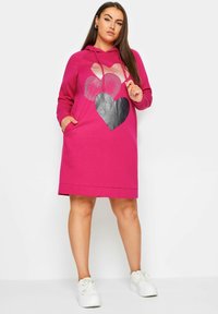 Vaaleanpunainen hupparimekko etutaskulla, jossa on kolme sydänkuviota, jotka on toteutettu glitter- ja matta finishillä. Yhdistetty valkoisiin lenkkareihin.