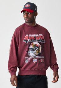 Bordová mikina se znakem "San Francisco 49ers", logy NFL a detaily Super Bowlu. Doplněná šedou a červenou čepicí.