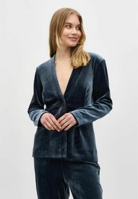 Donkerblauwe fluwelen blazer met een diepe V-hals, enkele knoopsluiting, lange mouwen en een zachte textuur; gecombineerd met bijpassende broek.