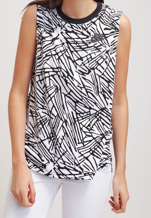 Bezrekawnik Nike z abstrakcyjnym wzorem linii w kolorze czarnym i białym, noszony z białymi spodniami, widoczny od ramion do bioder.