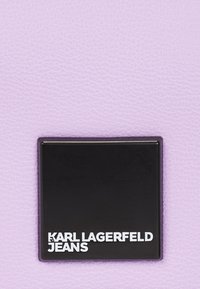 Lavender textured leather with a matte black square label displaying "KARL LAGERFELD JEANS" in white sans-serif font.