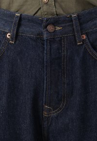 Mørkeblå denim jeans med kontrasterende orange syninger, der har en knaplukning, fem lommer og en glat tekstur.