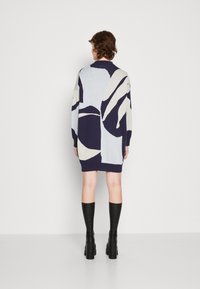 Abito maglione in maglia con motivi astratti blu navy e azzurri, maniche lunghe, colletto alto e orlo a coste, abbinato a stivali neri fino al ginocchio.