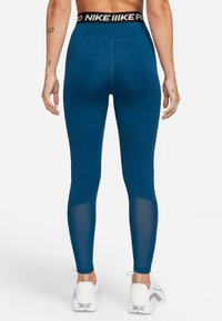 Blå sportiga leggings med en svart märkesmidja. Har nätpaneler längs med de nedre benen och ett mjukt, stretchigt tyg.
