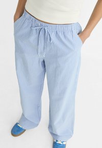 Pantalons rayés bleu clair avec une taille à cordon, jambes larges et poches latérales, fabriqués en tissu léger.
