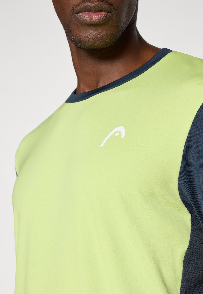 Camiseta deportiva verde claro con detalles en azul marino, cuello redondo, mangas cortas y un logo sutil en el pecho. La tela texturizada añade un toque especial.