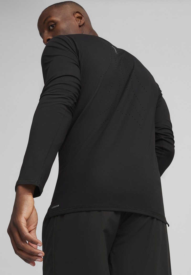 Langärmliges schwarzes Sportshirt mit glatter Textur, das ein durchlöchertes Muster auf dem Rücken und ein Logo-Detail in der Nähe des Saums aufweist.