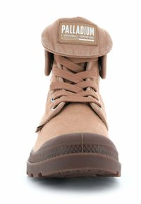 Bottes en toile marron à la cheville avec un bout renforcé, des lacets plats, une semelle en caoutchouc et un col pliable arborant un patch logo sur la languette.