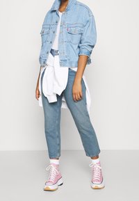 Džínová bunda s vybledlou světle modrou barvou, dvěma náprsními kapsami, doplněná o světle modré dž íny a růžové vysoké tenisky s bílými podešvemi.