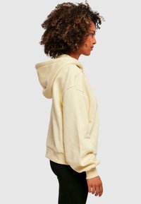Sudadera con capucha de color amarillo claro, con un corte relajado, puños y dobladillo acanalados. Tela suave, bolsillo tipo canguro en la parte delantera. Diseño sencillo.