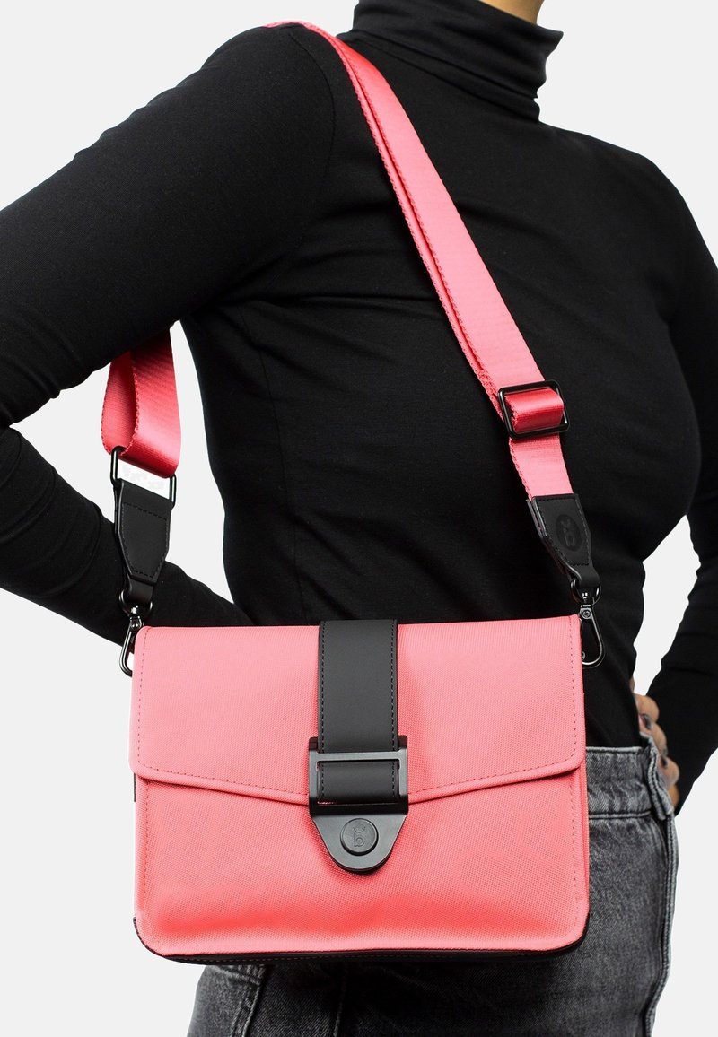 Umhängetasche aus leuchtend pinkem Textil, mit einem schwarzen Lederumschlag, verstellbarem Trageriemen und Druckverschluss. Kompakte rechteckige Form.