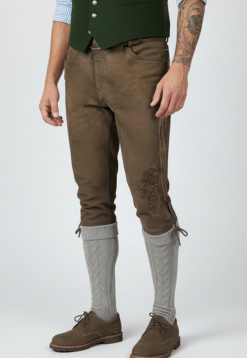 Hnědé, úzce střižené kalhoty s texturovaným povrchem. Obsahují dekorativní výšivku na straně, kombinované s pletenými šedými návleky na nohy a hnědými botami.