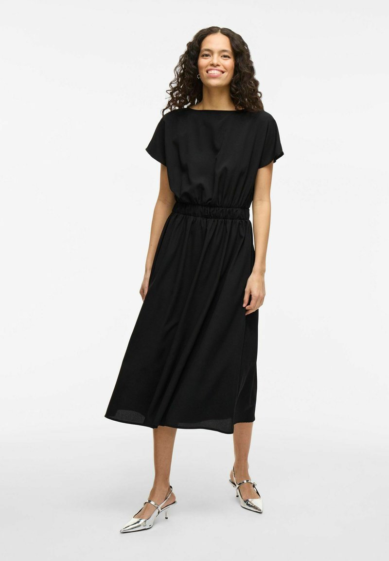 Black midi dress with short sleeves, elastic waist, and flowing design. Paired with silver slingback heels. Smooth fabric texture.