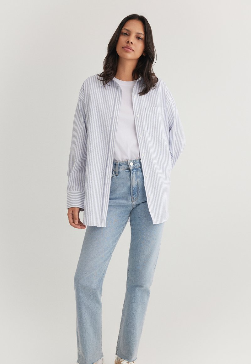 Light blue and white striped button-up shirt with a relaxed fit, single chest pocket, and long sleeves, paired with light wash straight-leg jeans.