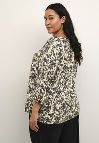 Blusenshirt mit Blumenmuster in Creme, Schwarz und Grün. Mit 3/4-Ärmeln im Glockenstil, lockerer Passform, rundem Halsausschnitt und weichem Material.