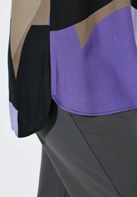 Meer gekleurde blouse met zwarte, bruine en paarse geometrische patronen, met een gladde textuur en afgeronde zoom, gecombineerd met grijze broek.