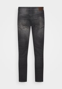 Jeans de denim negro de corte ajustado con una textura desgastada, que presentan un parche de cuero marrón en la cintura y dos bolsillos traseros.