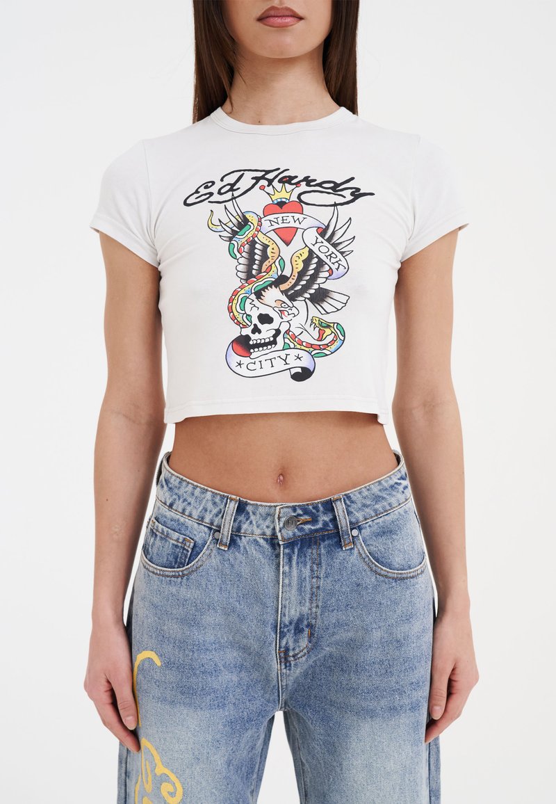 Hvid, kortærmet t-shirt med et farverigt grafisk motiv, der viser designs af et kranium, en ørn og en slange. Sættes sammen med lyseblå denim jeans.