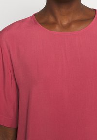 Kortärmad topp i en dämpad rosa färg, gjord av mjukt tyg, med rund halsringning och en slät yta, lämplig för vardagsbruk.