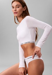 Top corto bianco a maniche lunghe e slip abbinato con il logo nero "Calvin Klein" sulla cintura elastica e un design liscio e attillato.