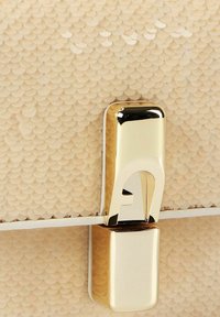 Borsa beige con motivo a squame testurizzate. Presenta una chiusura metallica dorata e una tracolla bianca, con un design elegante e moderno.