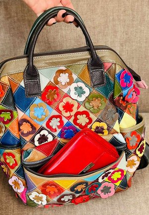 Hand holding a colorful patchwork leather bag with flower appliqués, front pocket unzipped showing a red leather wallet inside.