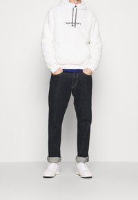 Felpa con cappuccio in pile bianco con logo "POLO SPORT", jeans scuri in denim e sneakers bianche. La felpa ha un cappuccio con coulisse e polsini a costine.