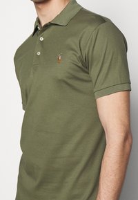 Olivgrön polo skjorta i en mjuk bomullsblandning, med treknappars placket och en liten broderad hästlogotyp på bröstet.