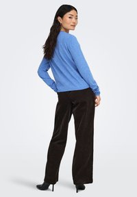 Blauwe trui met lange mouwen en gestructureerde stof, gecombineerd met donkerbruine fluwelen wijde broek. Zwarte hoge hakken benadrukken de outfit.