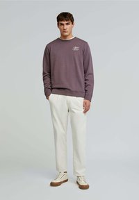 Felpa viola scuro con polsini e fondo a costine, caratterizzata da testo stampato bianco. Abbinata a pantaloni avorio e sneakers bianche con suola marrone.
