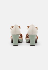 Sandales à talons en cuir crème avec talons texturés vert menthe, dos ouverts et brides de cheville avec garniture dorée.