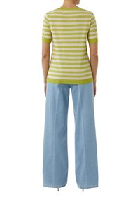 Sweter w paski, robiony na drutach, z krótkimi rękawami w zielono-białym kolorze, w połączeniu z luźnymi jasnoniebieskimi dżinsami, podkreślającymi swobodny krój.