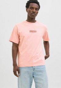 Světle růžové bavlněné tričko s krátkými rukávy, na hrudi se nachází nápis "ORIGINALS SUMMER EDITION" v tmavším písmu.
