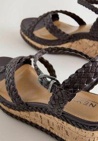 Sandales compensées en cuir tressé marron avec fermeture à boucle et semelles plateforme en liège, détails en gros plan des brides et de la texture.