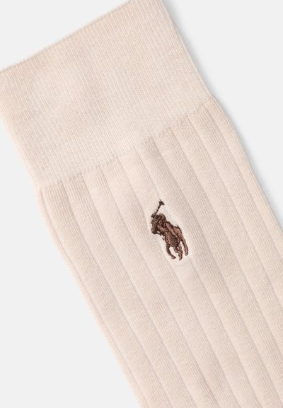 Calzino beige a costine con un motivo texturizzato, dotato di un logo ricamato marrone vicino alla parte superiore. Tessuto morbido, lunghezza media sul polpaccio.