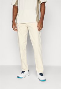Cream-colored pants with a tailored fit, paired with a light beige and white shirt, complemented by white sneakers with blue accents.